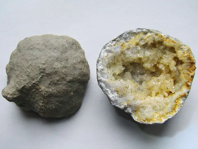 Two geodes side by side: a round, lumpy gray rock and a broken one with a white shell lined with pale yellow crystals